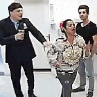 a man in a suit is standing next to a woman and a man in a black shirt .