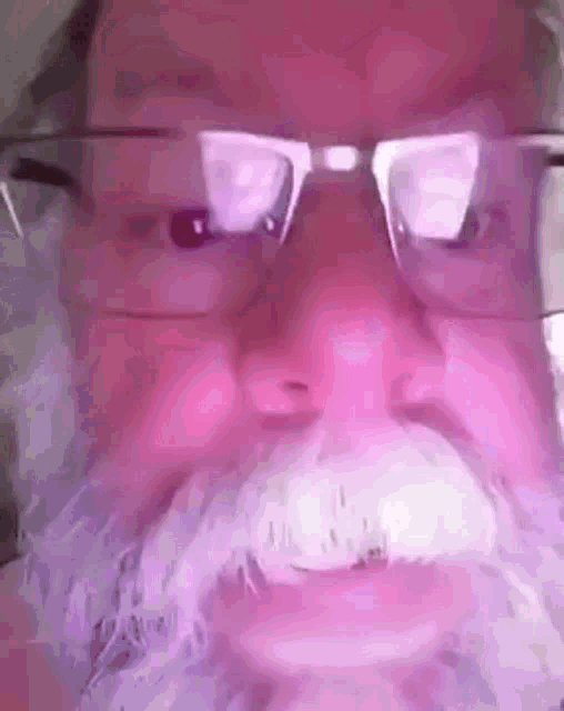 a man with glasses and a white beard is wearing a santa claus costume .
