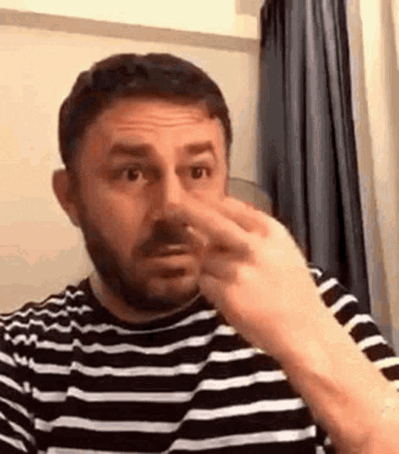 a man with a beard wearing a striped shirt is covering his nose with his hand .