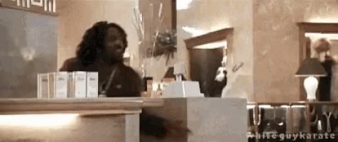 a man stands behind a counter in a room with the words white guykarate on the bottom right