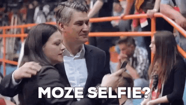a man in a suit is taking a selfie with a woman in a crowd .