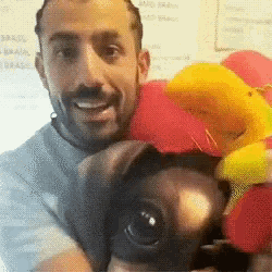 a man is holding a stuffed animal and smiling in front of a sign that says amg brasil