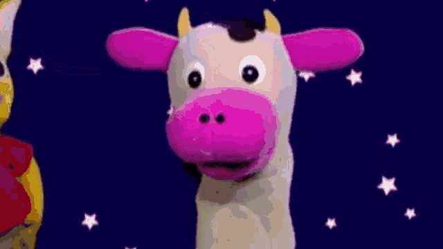 a puppet of a cow with pink ears and horns is standing in front of a blue sky with stars .