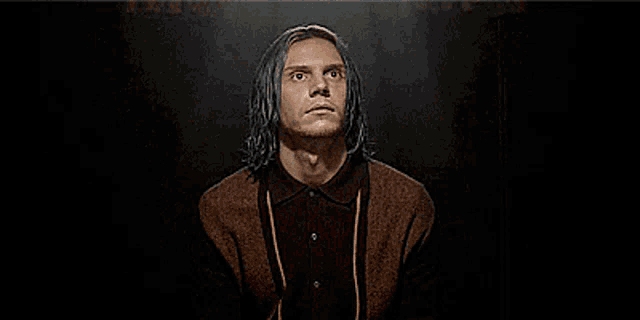 a man with blue hair is wearing a brown shirt and a brown cardigan .