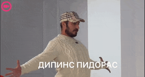a man with a beard wearing a hat and a sweater with russian writing behind him