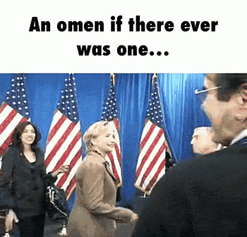 a picture of hillary clinton standing in front of american flags and a caption that says an omen if there ever was one