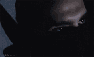 a man wearing a black mask is holding a microphone in his hand in the dark .