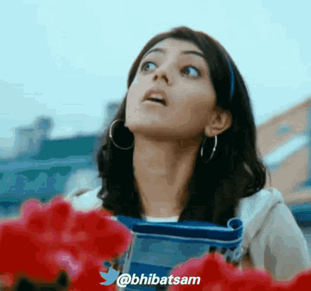 a woman is looking up at the sky with flowers in the foreground and a twitter logo in the lower right corner