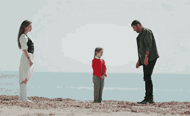 a man in a green jacket stands next to a woman and a little girl on a beach