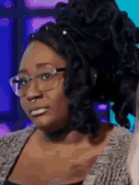 a woman wearing glasses and dreadlocks is looking at the camera .