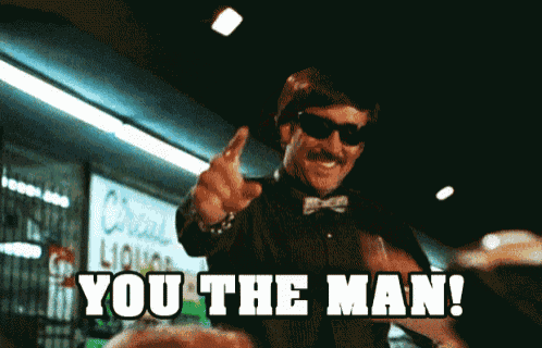 a man wearing sunglasses and a bow tie says " you the man " in front of a liquor store