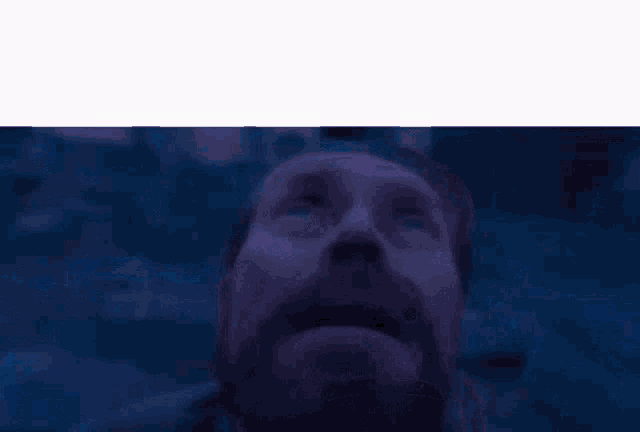 a man with a beard and mustache is looking up at the sky in a dark room .