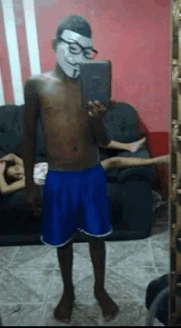 a shirtless man wearing a mask taking a selfie in front of a mirror .