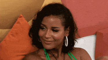 a woman wearing hoop earrings and a green bikini top smiles