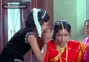 two women are standing next to each other in a room . one of the women is putting flowers in the other 's hair .