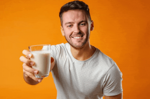 a man is holding a glass of milk in front of an orange background
