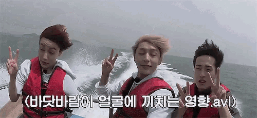 a group of young men are sitting on a boat in the ocean and giving peace signs .