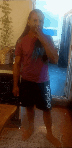 a man wearing a pink shirt and black shorts with the word adidas on the side