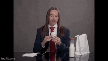 a man with long hair and a mustache is sitting at a table with a bottle of milk and a paper bag .