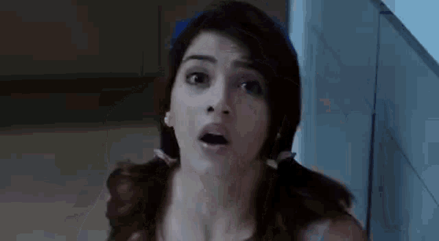 a woman with pigtails is standing in a bathroom and looking at the camera .