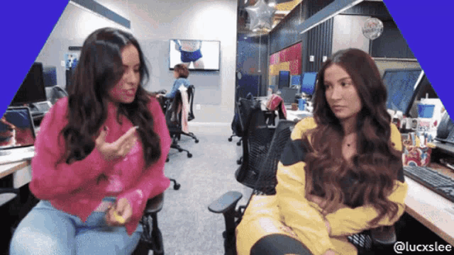 two women sit at a desk in an office with a blue border that says luckslee on it