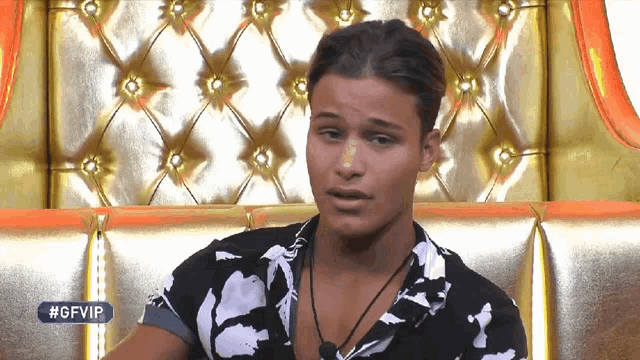 a man in a black and white shirt is sitting in front of a gold couch with #gfvip written on the bottom