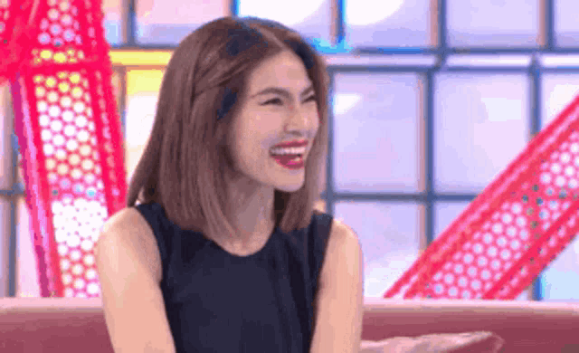 a woman in a black dress is sitting on a couch and laughing .