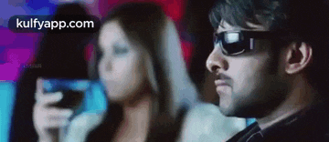 a man wearing sunglasses is sitting in a theater with a woman holding a cell phone .