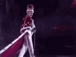 a man in a crown and robe is holding a cane and a microphone .