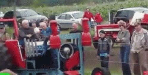 a group of people are standing around a red tractor .