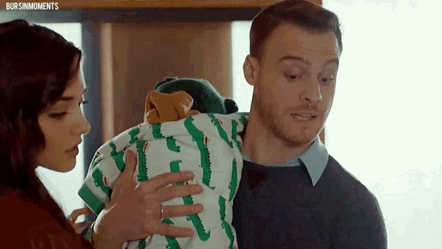 a man and a woman are holding a baby in a green outfit with crocodiles on it .