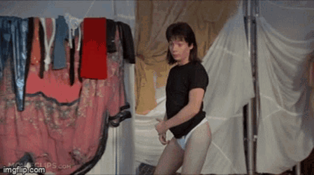 a man in a black shirt and white underwear is standing in front of a clothes line