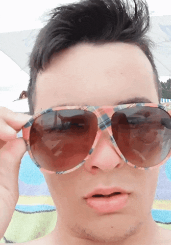 a man wearing plaid sunglasses looks at the camera with a surprised look on his face