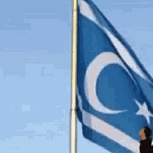 a man is standing in front of a blue and white flag with a crescent moon on it .