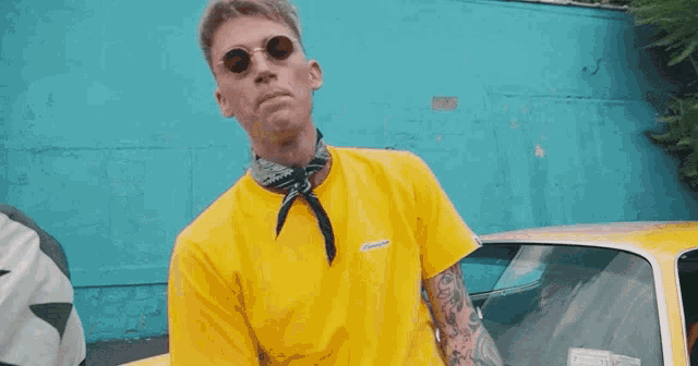a young man wearing sunglasses and a yellow shirt is standing in front of a blue wall .