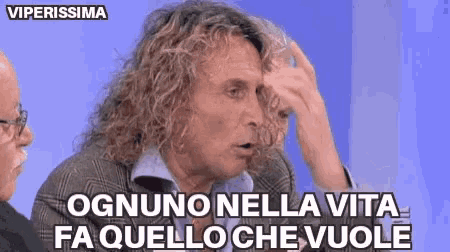 a man with curly hair is making a funny face and says ognuno nella vita fa quello che vuole .