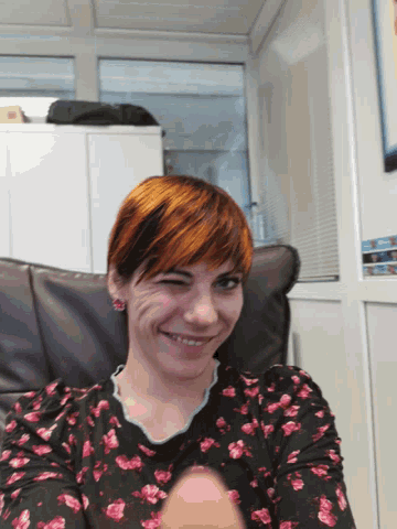a woman with red hair is smiling and wearing a black and pink floral shirt