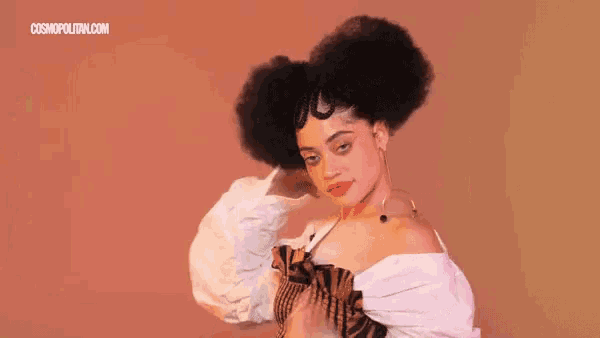 a woman with a large afro is wearing a white top and earrings .
