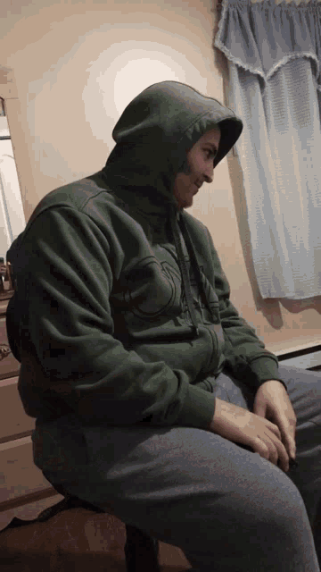a man wearing a green hoodie is sitting in front of a window