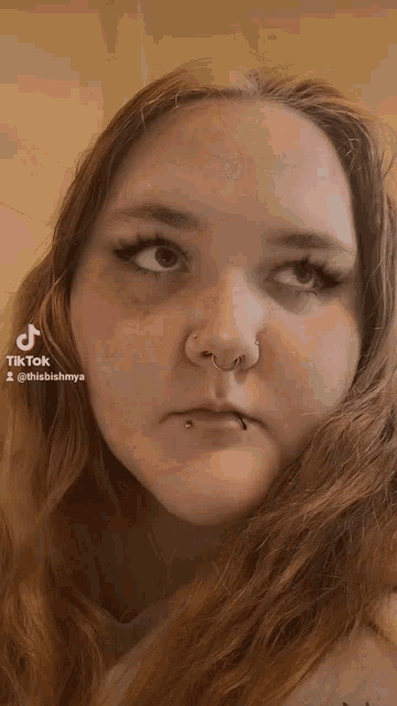 a woman with a nose ring and a lip piercing looks up at the camera