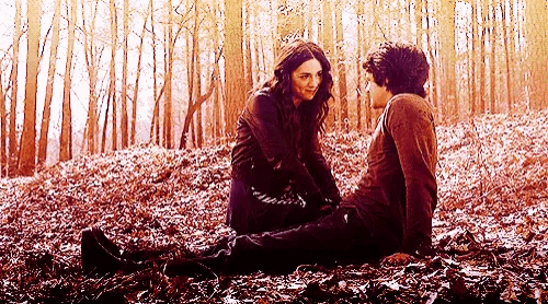 a man and a woman are sitting in a pile of leaves in a forest