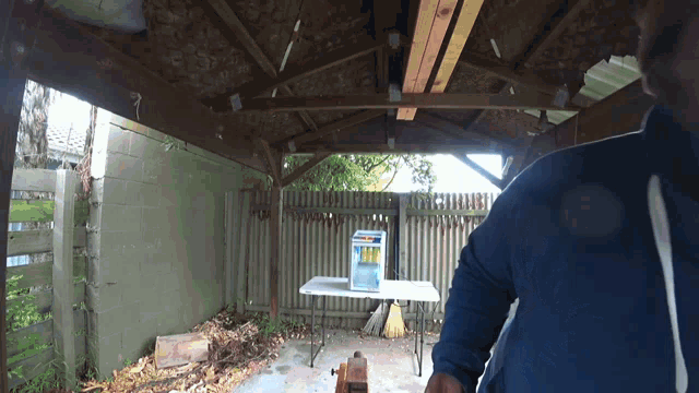 a man in a blue jacket stands in front of a fence and a table