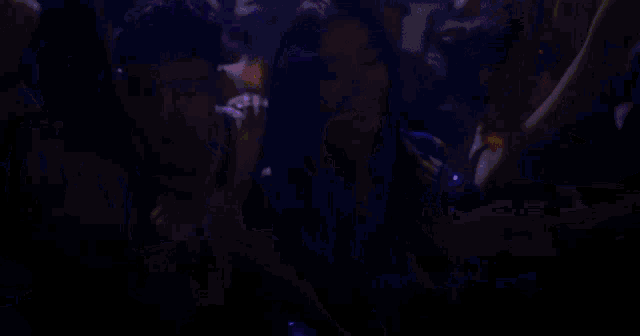 a crowd of people are dancing in a dark room with purple lights