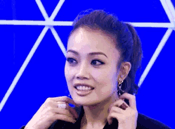 a close up of a woman adjusting her earrings with a blue background