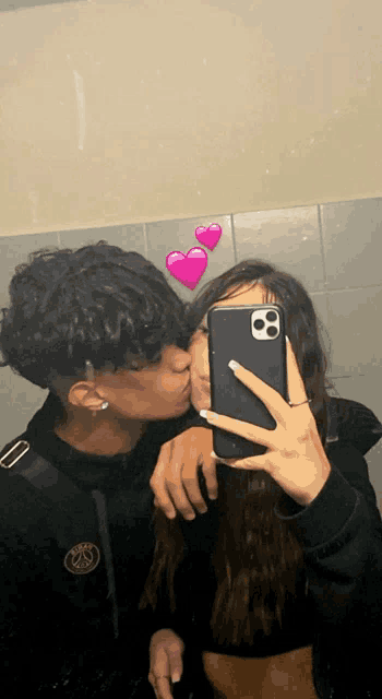 a man kisses a woman on the cheek while taking a selfie with his phone