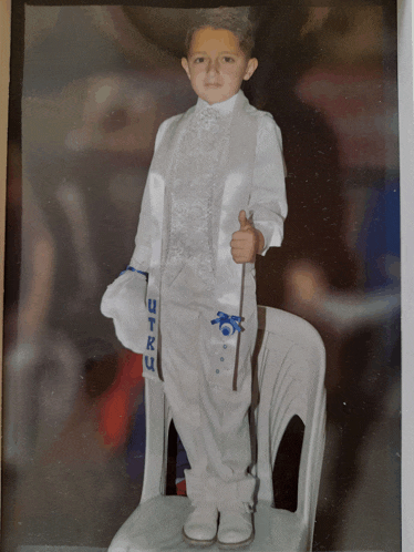 a young boy in a white suit is giving the thumbs up sign
