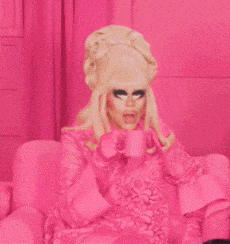 a woman in a pink dress is sitting on a pink couch in front of a pink wall .