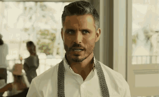 a man with gray hair and a beard wearing a white shirt and suspenders is looking at the camera .