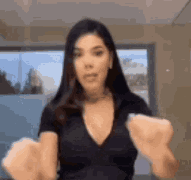 a woman in a black shirt is making a fist with her hands in front of a window .