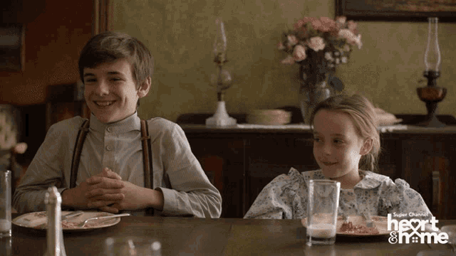 a boy and a girl are sitting at a table with a heart & home logo in the corner